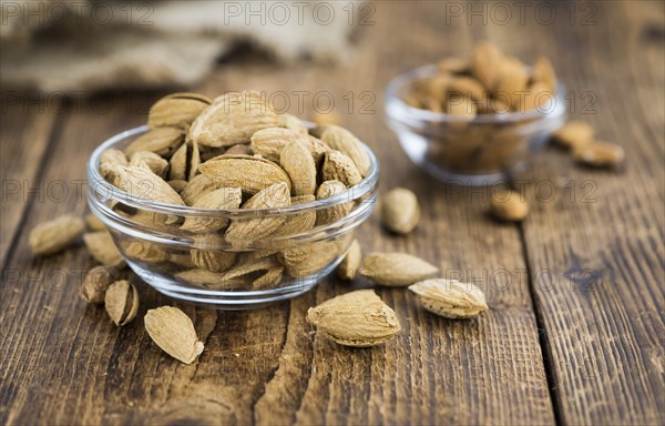 Roasted Almonds (in shell) on an old wooden table (close-up shot, selective focus)