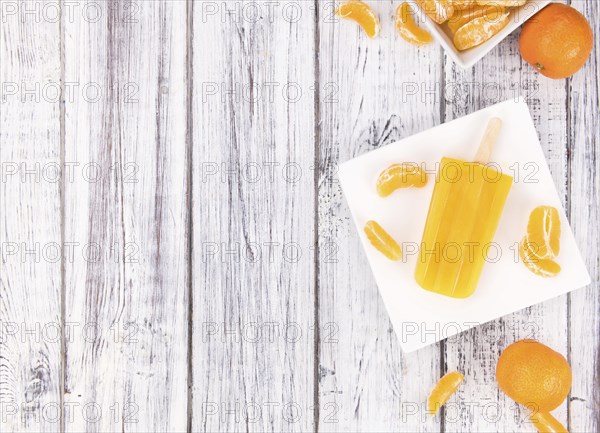 Old wooden table with a portion of homemade Tangerine Popsicles (selective focus, close-up shot)