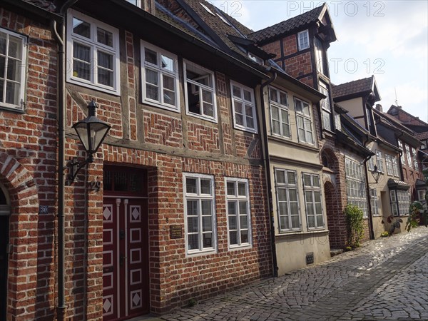 The photo shows a well-kept street with historic brick houses and nostalgic lamps along the cobbled street, lüneburg, germany