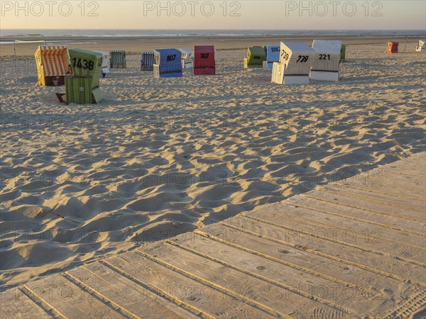 A wooden promenade leads past colourful beach chairs on the quiet sandy beach, langeoog, germany