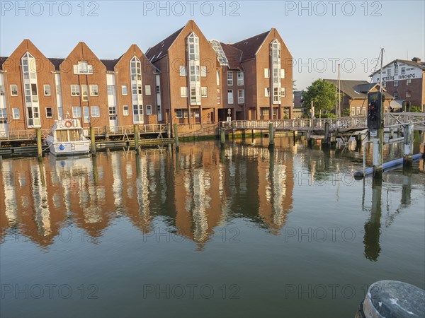 Brick buildings and jetties are reflected in the calm waters of the canal, a few boats can be seen, husum, schleswig-holstein, germany