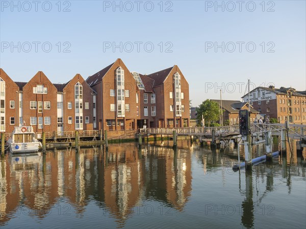 Brick houses radiating tranquillity and a jetty are reflected in the water of the canal, the sky is clear, husum, schleswig-holstein, germany