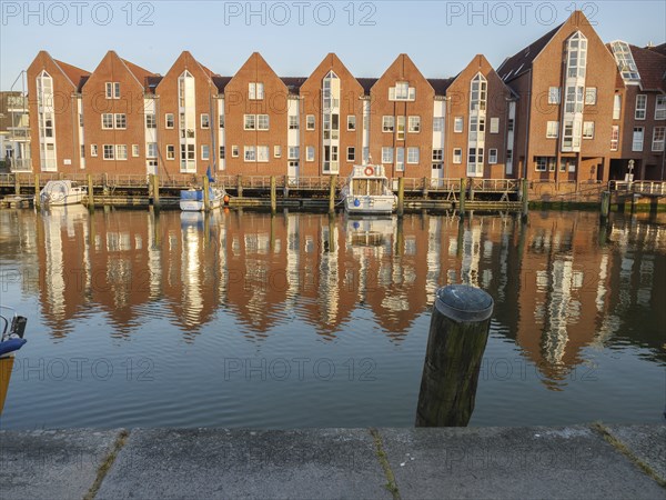 Brick houses are reflected in the calm waters of a canal, jetties and boats are visible, husum, schleswig-holstein, germany