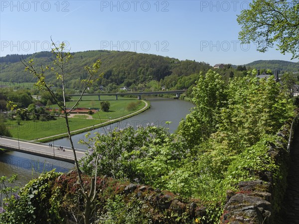 River flows through green landscape, surrounded by hills and bridge, saarburg, germany