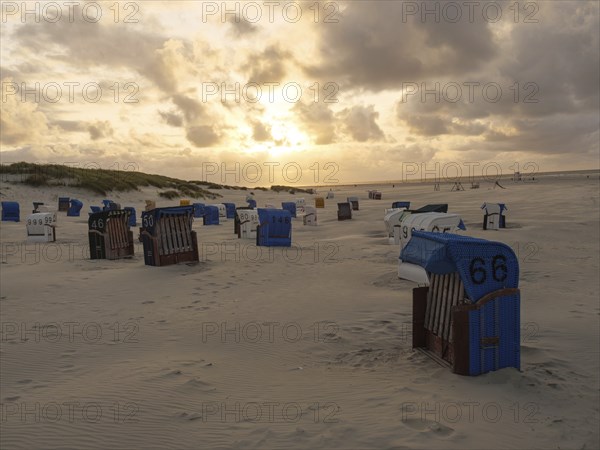 Beige sandy beach at sunset with scattered colourful beach chairs and dramatic sky, Juist, North Sea, Germany, Europe