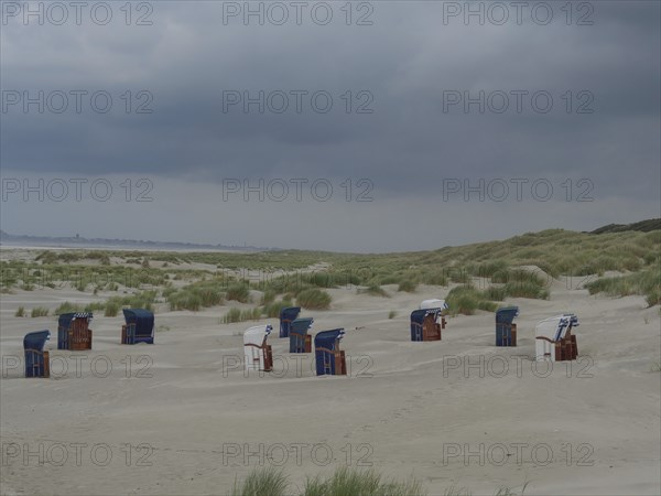 Scattered beach chairs on a sandy beach between grass and dunes under threatening clouds, Juist, North Sea, Germany, Europe