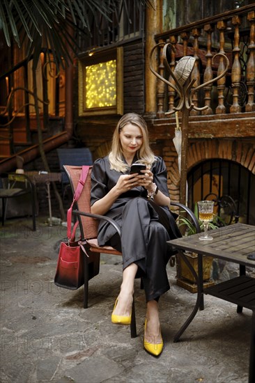A stylish woman came to a wine bar, sat on the terrace and writes a message to her friends on her smartphone that she is waiting for them