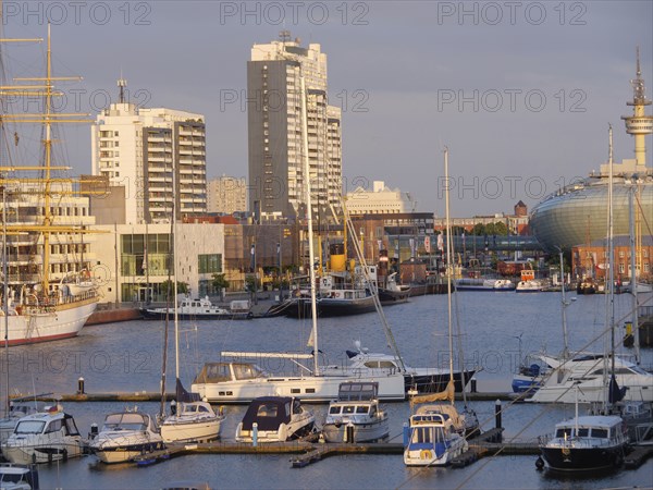 Harbour view with several yachts and boats in front of a city backdrop of skyscrapers in the evening light, bremerhaven, bremen, germany