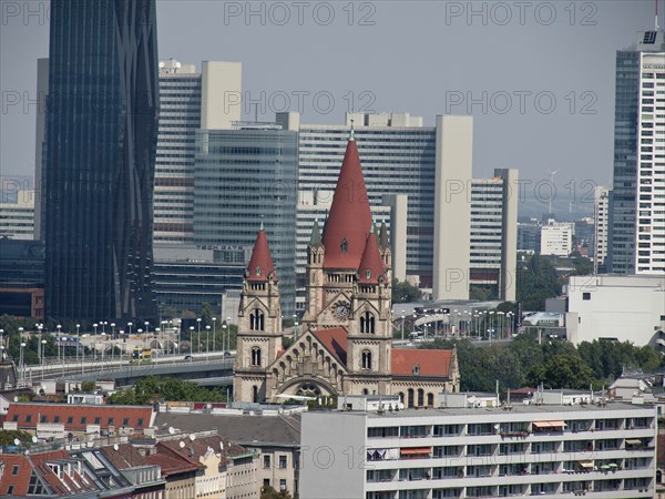 A church with red roofs in front of modern skyscrapers in an urban environment on a sunny day, Vienna, Austria, Europe