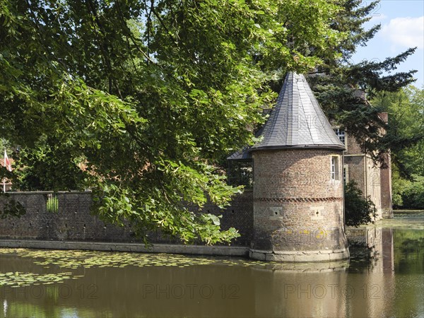 Brick round tower with grey roof, surrounded by a moat and summer greenery, view of historic buildings, ochtrup, münsterland, germany
