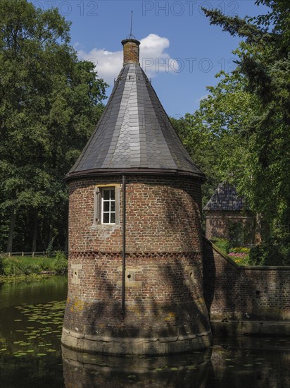 Brick round tower with lead-grey roof on a moat, surrounded by summer nature, ochtrup, münsterland, germany