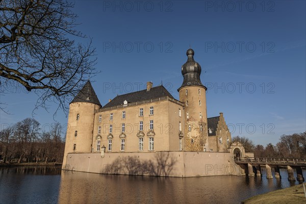 Castle with moat and striking helmet tower surrounded by winter trees on a bright day, gemen, münsterland, germany