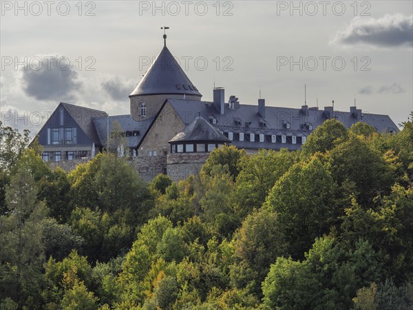 An old castle with towers surrounded by autumnal forests under a cloudy sky, Waldeck, Hesse, Germany, Europe