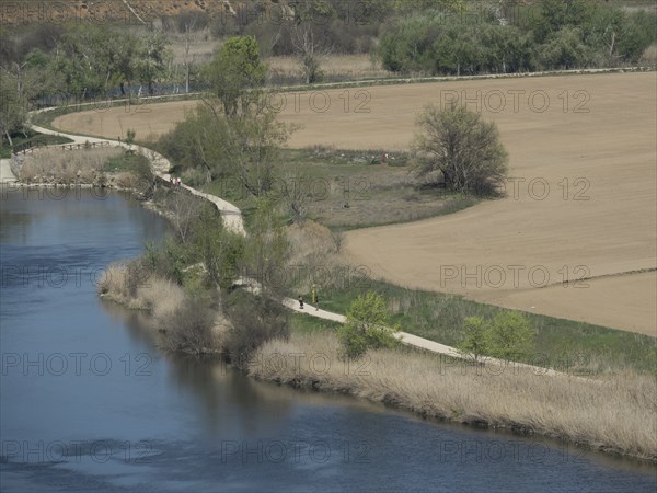 A nature shot of a winding path along a riverbank with trees and fields, toledo, spain
