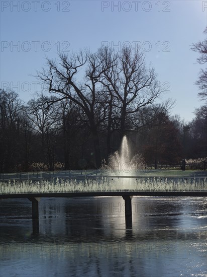 Fountain in a wintry park, surrounded by bare trees and reflecting water under sunlight, ruurlo, gelderland, the netherlands