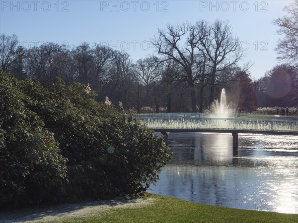 A fountain in the park, surrounded by water and bare trees in the winter sunlight, ruurlo, gelderland, the netherlands