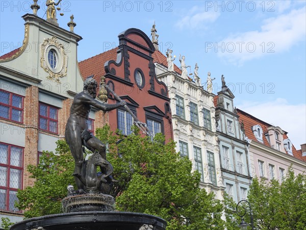 Statue of a fountain in front of a row of historic, decorated houses and green trees in a cloudy sky, Gdansk, Poland, Europe