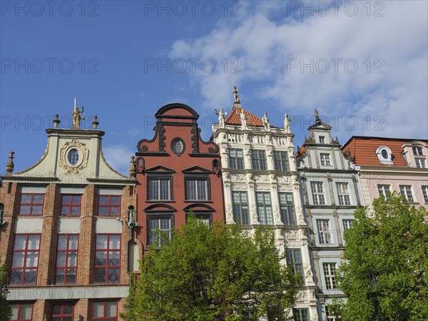 Decorated historic houses with trees in the foreground against a partly cloudy sky, Gdansk, Poland, Europe