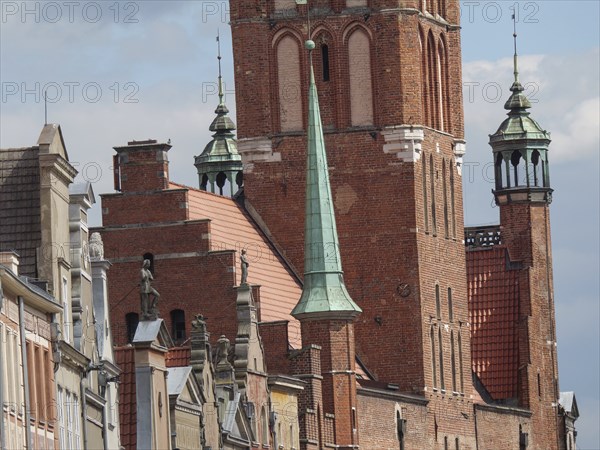 A Gothic church tower made of red bricks with stone statues on nearby historic buildings, Gdansk, Poland, Europe