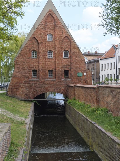 Stone bridge with an old brick building above it, under which a canal flows, Gdansk, Poland, Europe