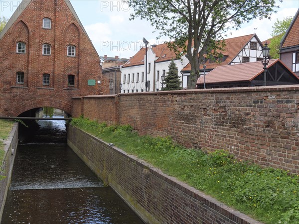 Canal flows under a brick bridge with neighbouring historic buildings and a stone wall, Gdansk, Poland, Europe