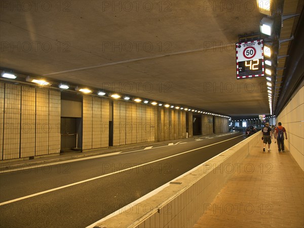 An illuminated tunnel with a road and pavements, people walking along the pavement, monte carlo, monaco, france