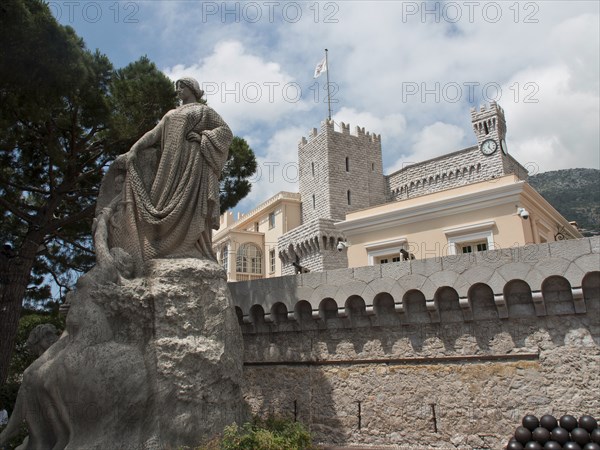 Statue in front of a castle with a clock tower, surrounded by trees and a cloudy sky, monte carlo, monaco, france