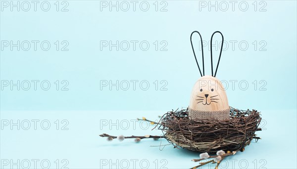Easter bunny or rabbit sitting in a bird nest, willow branches, wooden egg, spring holiday, brown and blue color