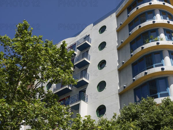 Modern residential building with round windows and balconies, green tree in the foreground, Lisbon, portugal