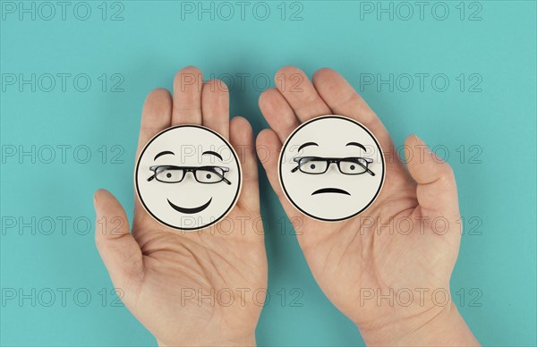 Holding a head with a sad and a happy face in the hands, mental health concept, positive and negative mindset, depression, support and evaluation symbol, emotion