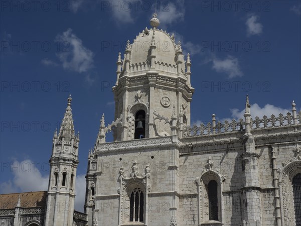 Large Gothic church facade with several towers and decorations under a blue sky with clouds, Lisbon, portugal
