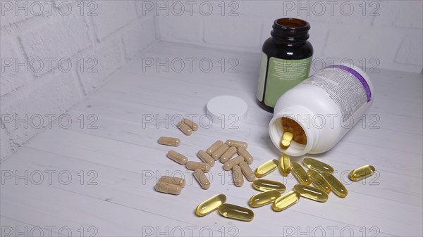 Scattered pills and capsules near two bottles on a white table against a brick wall