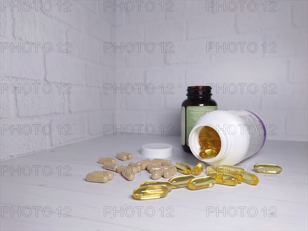 Opened supplement bottles with scattered pills and capsules on a white brick wall background