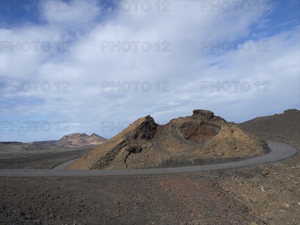 A winding tarmac road through a volcanic hilly landscape under an overcast sky, arrrecife, lanzaorte, canary islands, spain
