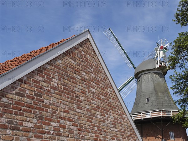 Brick building with the top of a windmill in the background under a blue sky, Greetsiel, East Frisia, Lower Saxony, Germany, Europe