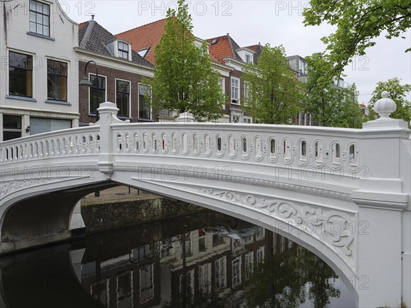 Decorative white bridge over a canal, surrounded by houses and green trees, Delft, Holland, Netherlands
