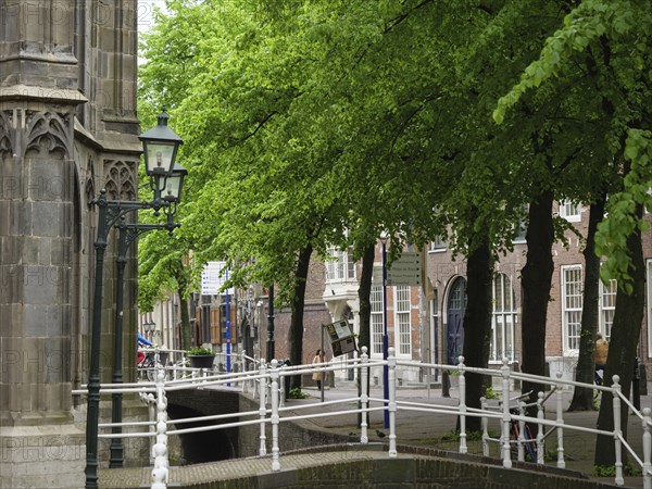 Historic buildings on a bridge over a canal, surrounded by green trees and lanterns, Delft, Holland, Netherlands