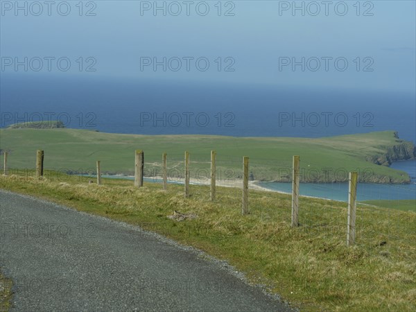 Road leading along a wooden fence overlooking a green island in the sea, lerwick, shetlands, scotland, uk