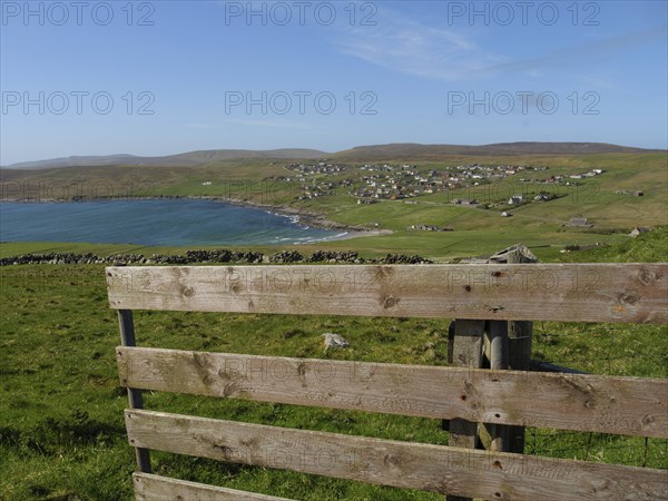 Wooden fence overlooking a coastline and a village surrounded by green hills under a blue sky with few clouds, lerwick, shetlands, scotland, uk