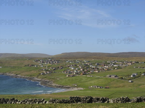 A coastal village scene with green fields and scattered houses under a clear sky, lerwick, shetlands, scotland, uk