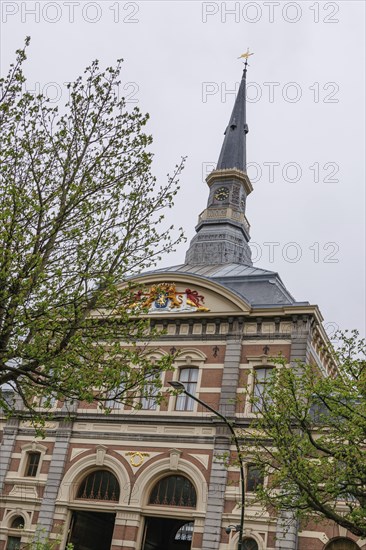Historic church tower rises above an ornate building view into the cloudy spring sky, The Hague, Netherlands