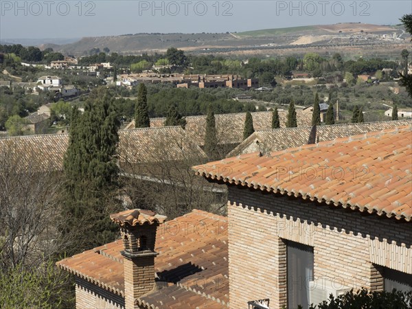 View of a hilly landscape with cypress trees and brick houses with a view over the roofs into the distance, Toledo, Spain, Europe