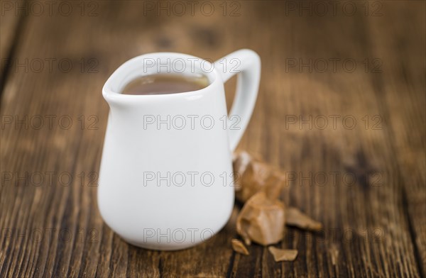 Caramel Syrup as high detailed close-up shot on a vintage wooden table (selective focus)