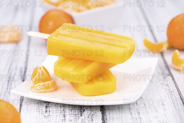 Old wooden table with a portion of homemade Tangerine Popsicles (selective focus, close-up shot)