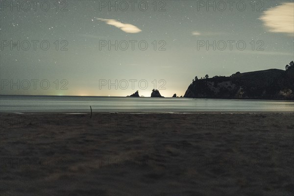 A beach at night with a calm sea atmosphere, starry sky and rocks, Whangamata, New Zealand, Oceania