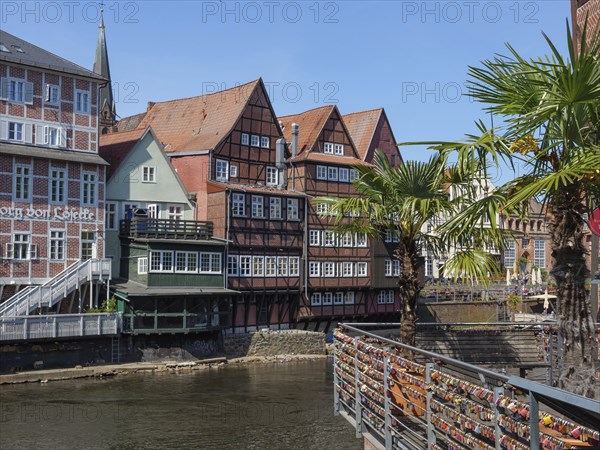 Idyllic view of half-timbered houses along a river, with a bridge and palm trees in the foreground, lüneburg, lower saxony, germany