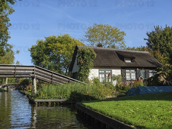 Small thatched house next to a wooden bridge on the river, surrounded by lush greenery, on a sunny summer's day, Giethoorn, Netherlands