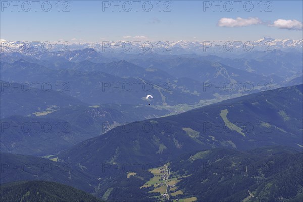 Aerial view of a mountainous landscape with a paraglider in the foreground under a clear sky, Gosau, Austria, Europe