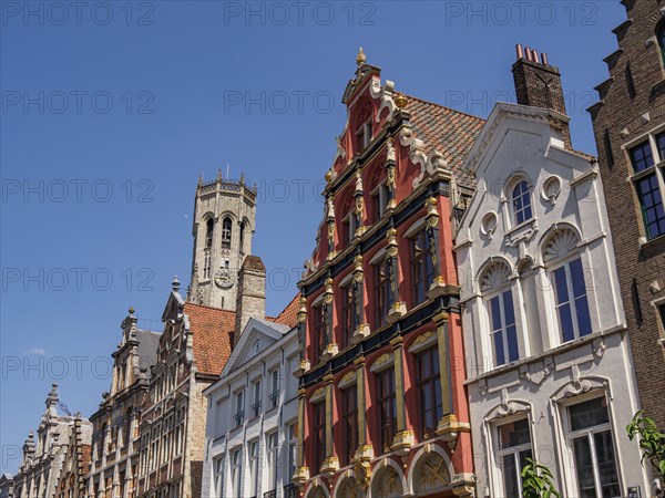 A historic street with stately brick buildings and a large tower in the background, Bruges, Belgium, Europe
