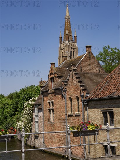 Picturesque scene with a canal, flowers and a bridge against the backdrop of a church tower, Bruges, Belgium, Europe